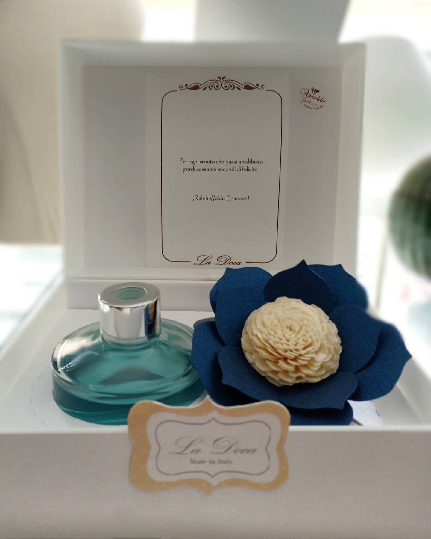 Una bottiglia di profumo, un fiore blu e una scatola, su un vassoio bianco. Sul retro c'è scritto