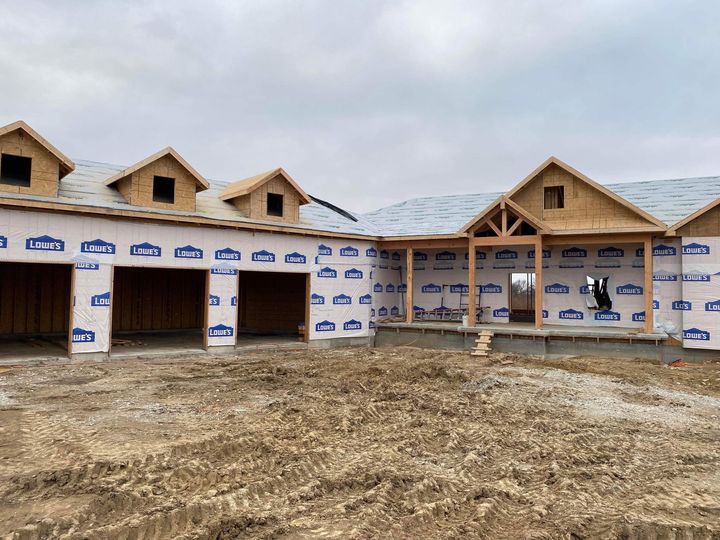 A large house is being built in the middle of a dirt field.