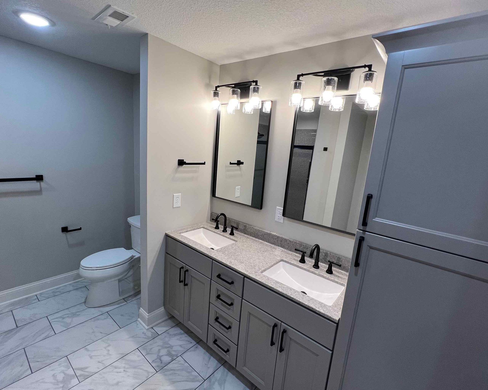 After renovation photo of a modern bathroom with sleek new fixtures, marble tiles, and improved lighting.