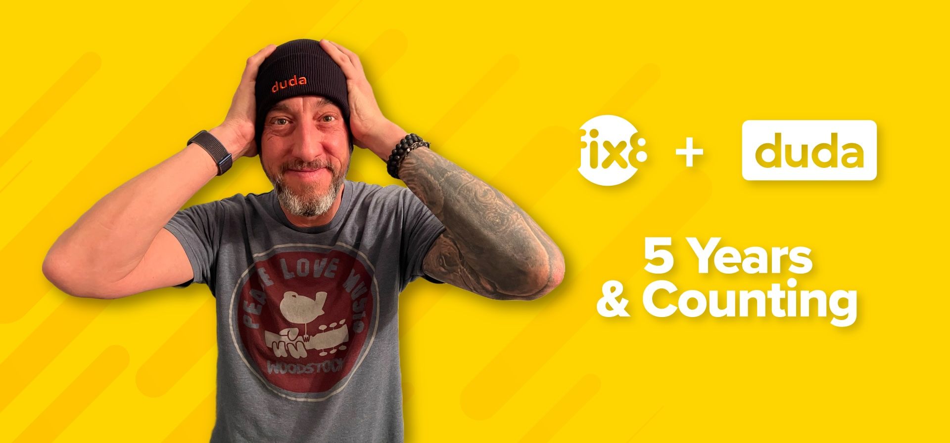 A man wearing a beanie and a t-shirt is covering his ears with his hands.