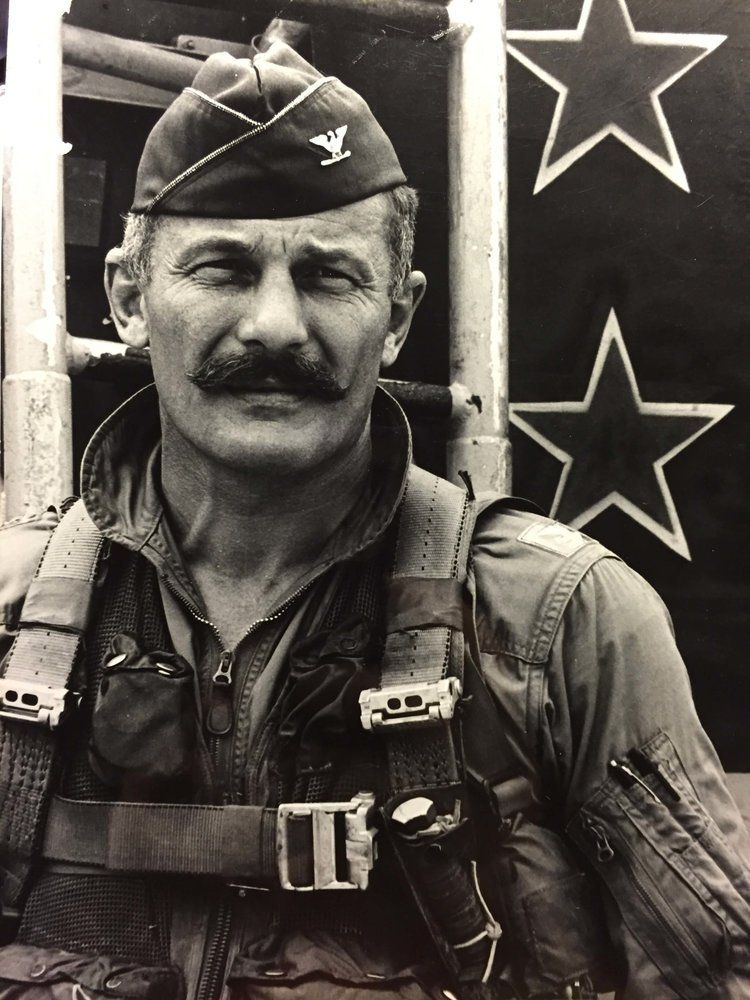 A man with a mustache wearing a hat with a bird on it