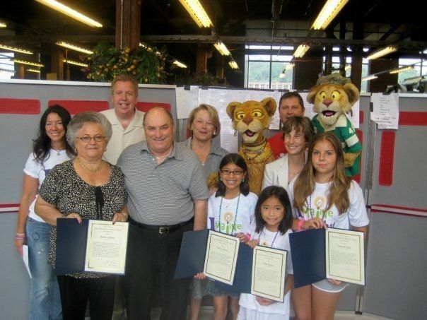A group of people holding certificates with a lion mascot in the background