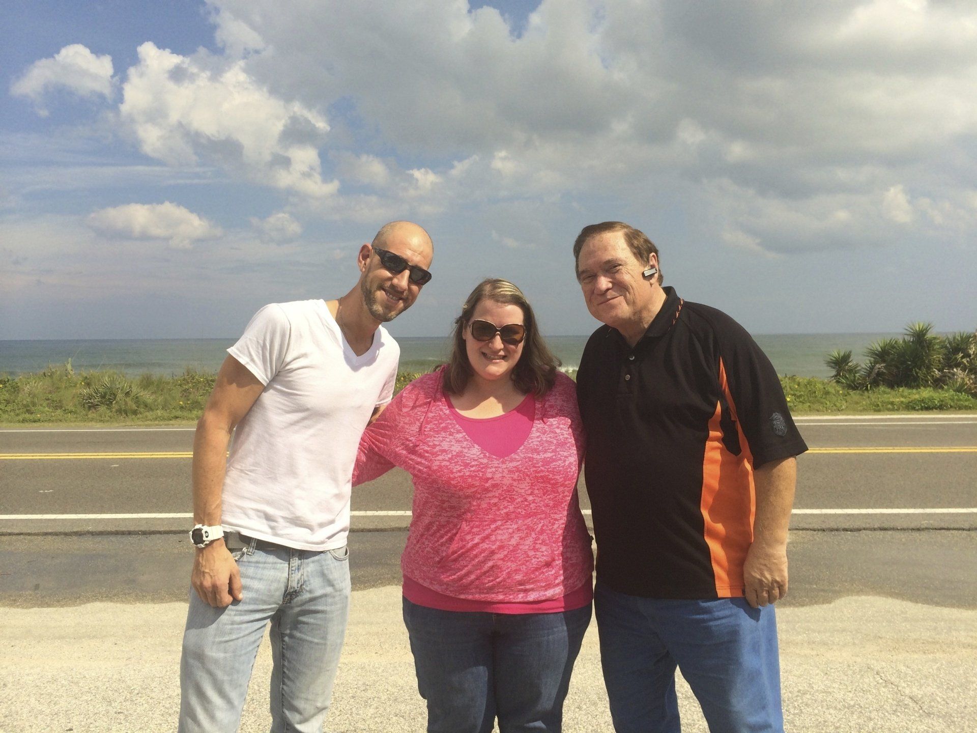 Three people are posing for a picture on the side of a road.