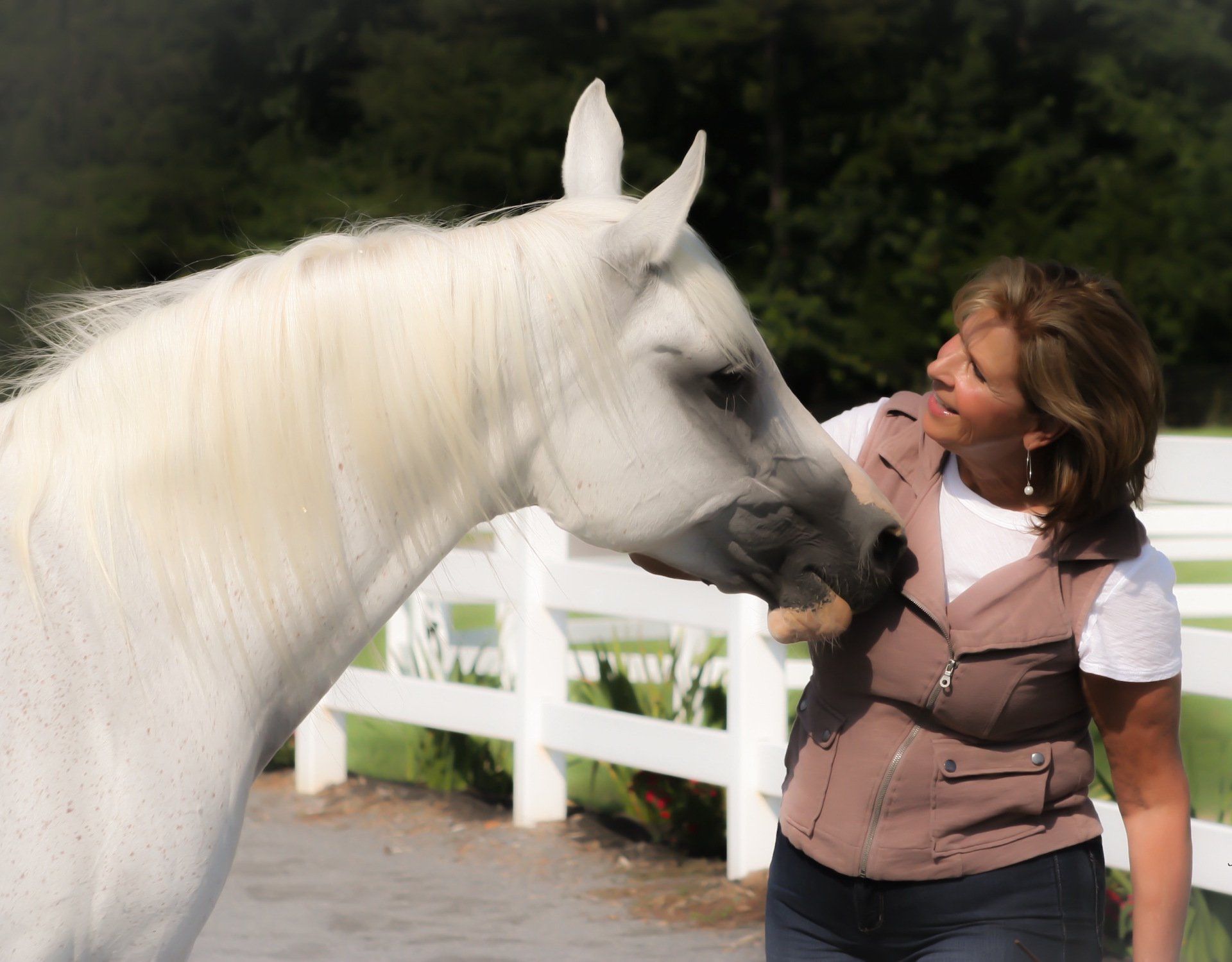 Woman petting a white horse's head outside near a white fence.