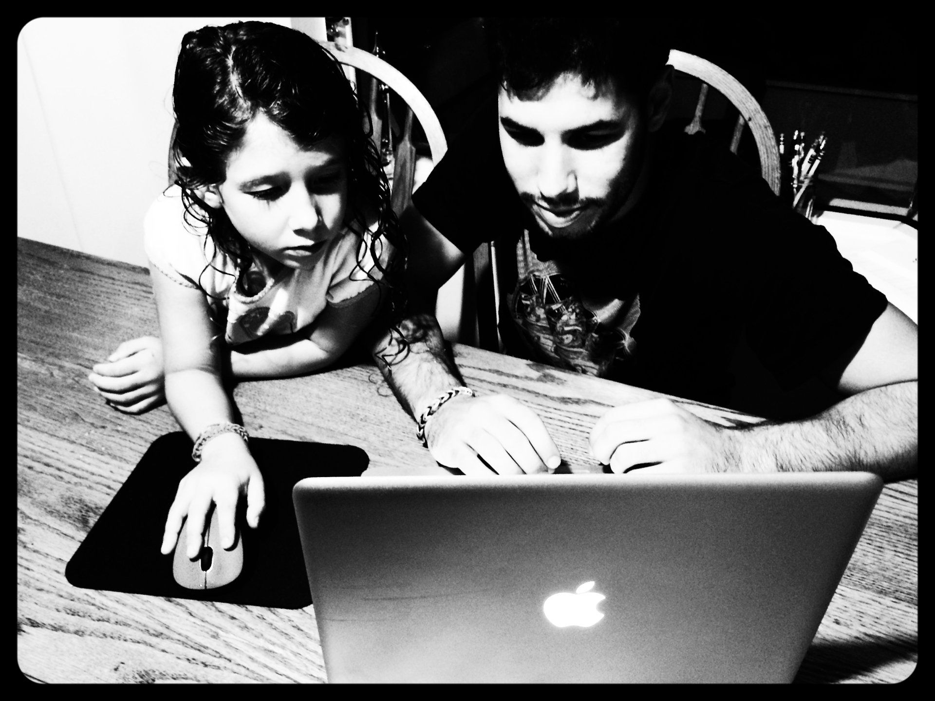 A man and a little girl are looking at an apple laptop