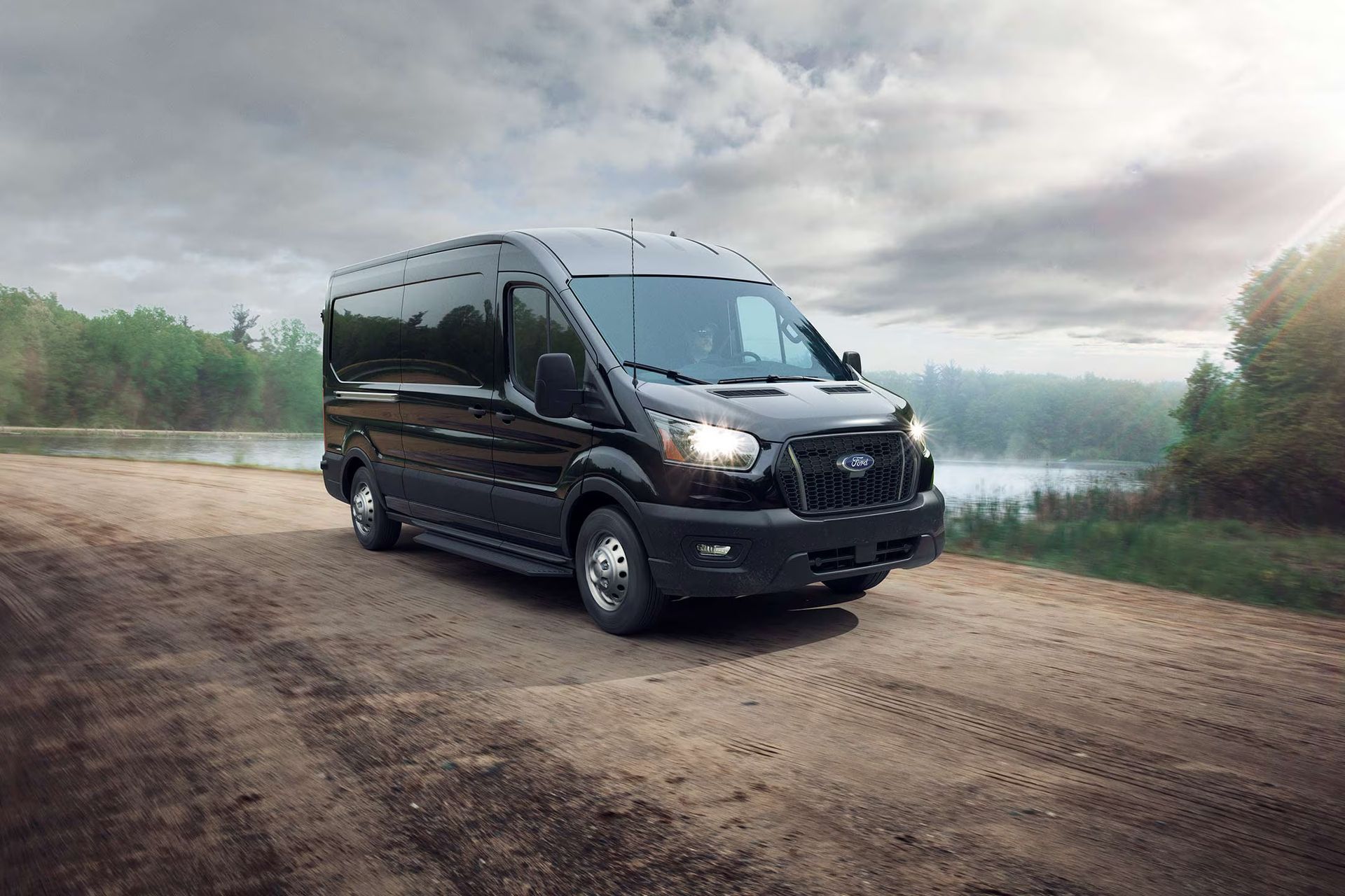 A black van is parked on a dirt road next to a lake.