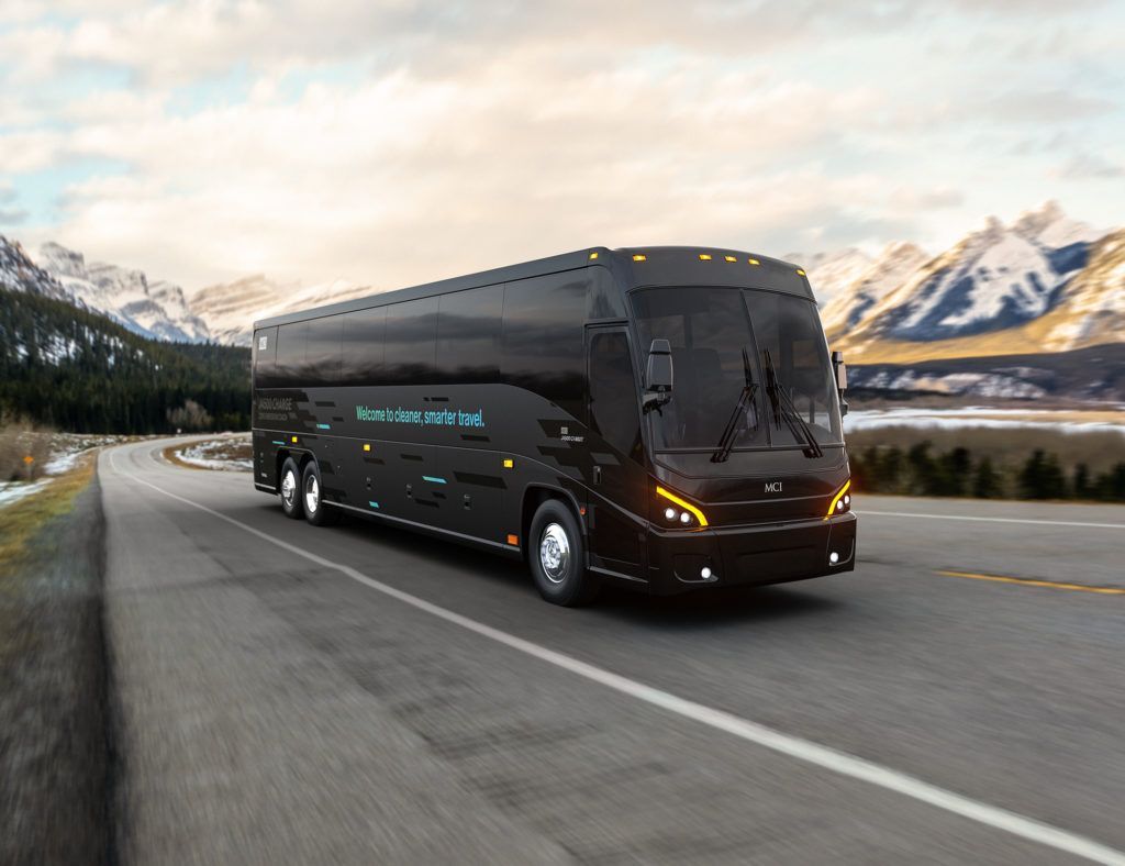 A black bus is driving down a road with mountains in the background.