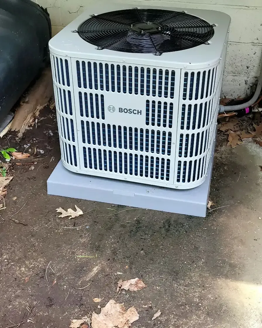 Bosch air conditioning unit on a gray base, outdoors on dirt and leaves.