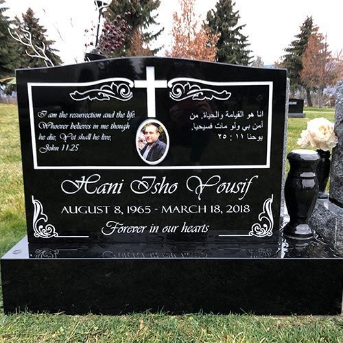 A black gravestone with a cross on it is in a cemetery.