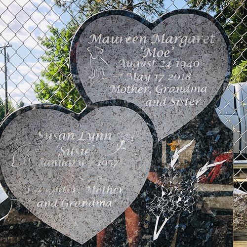 A gravestone with two hearts on it is behind a chain link fence.