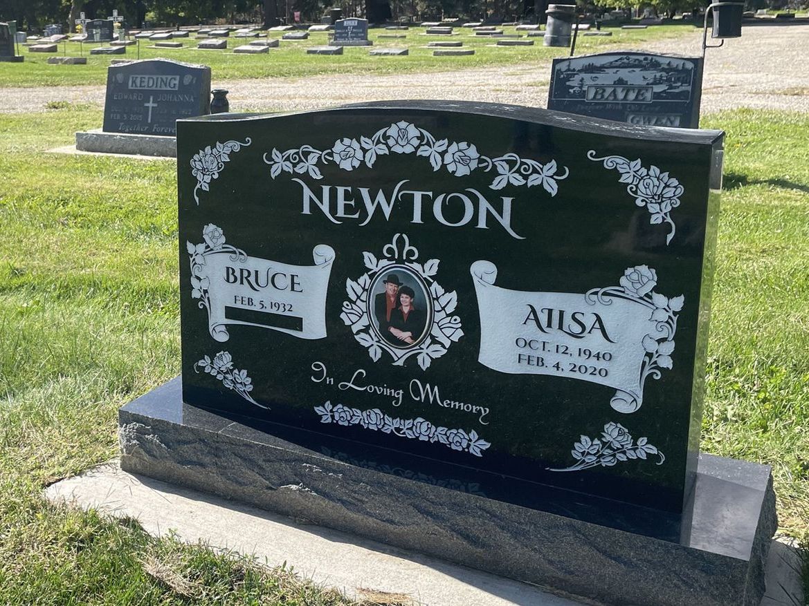 A black gravestone with the name newton on it is in a cemetery.