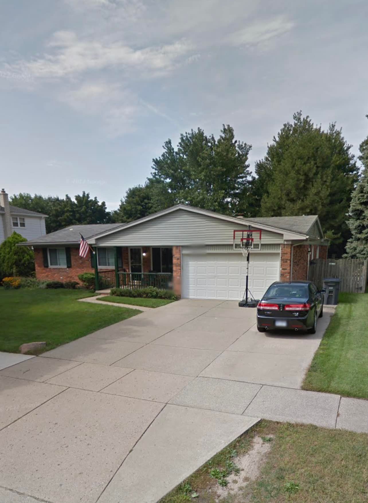 A car is parked in front of a house with a basketball hoop in the driveway