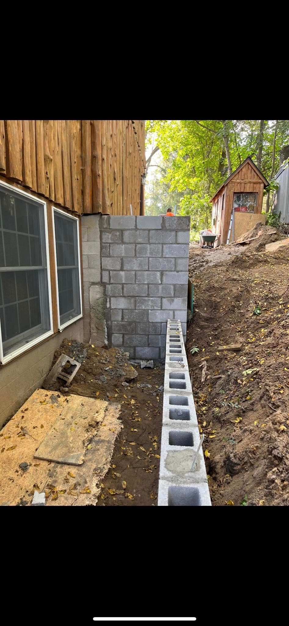 A brick wall is being built next to a house on a hill.