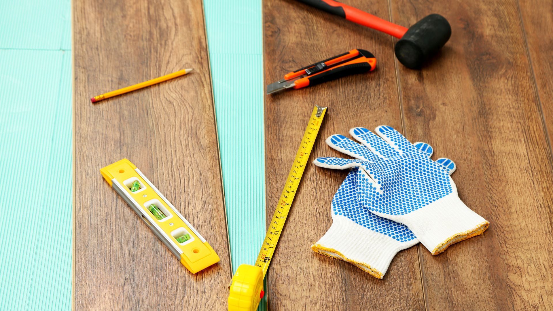 A pair of gloves , a tape measure , a level , and a hammer are on a wooden table.