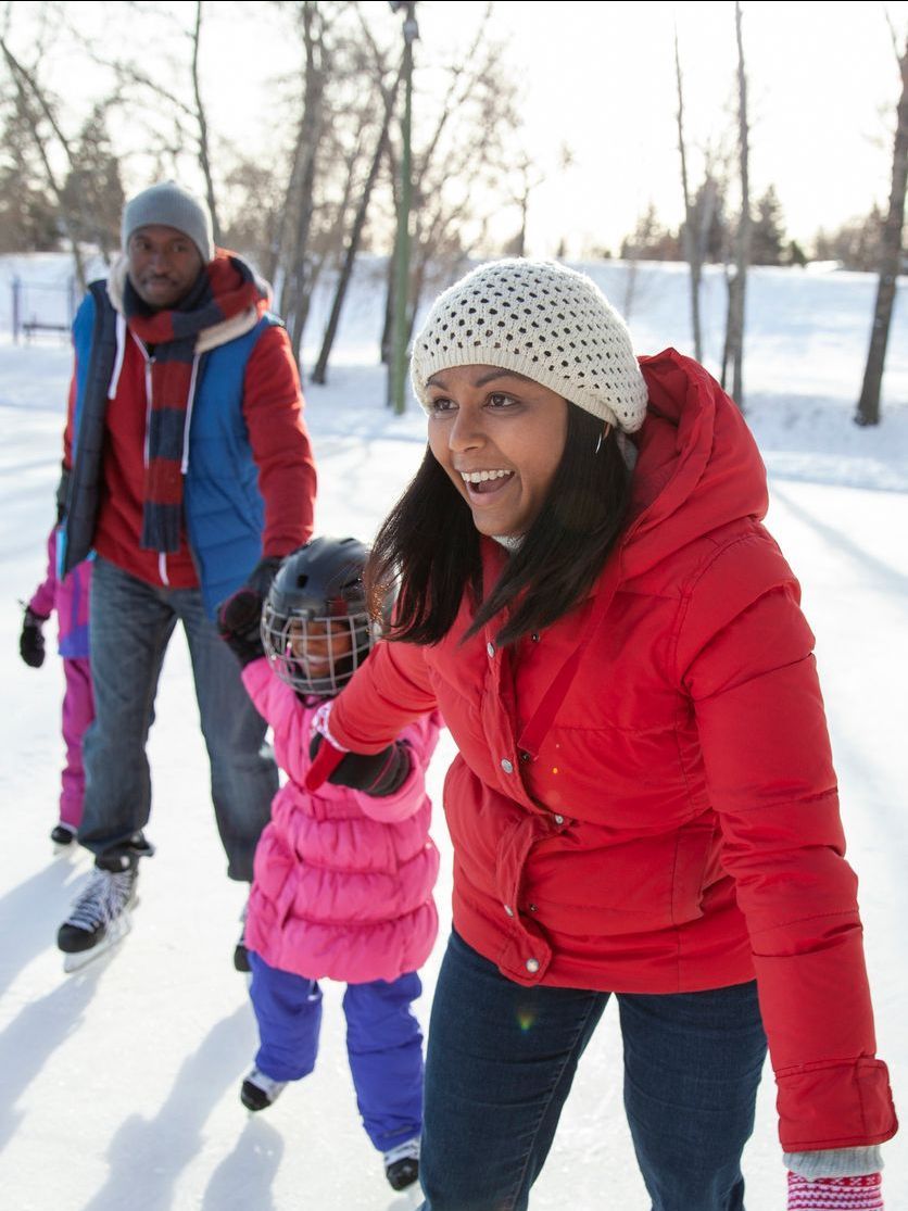 A woman in a red jacket is helping a little girl ice skate