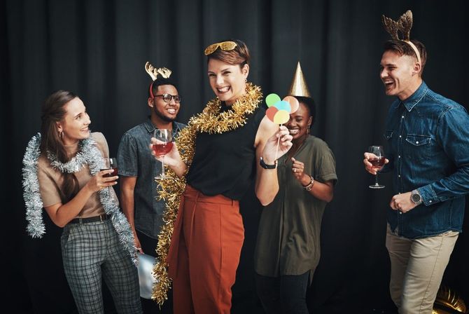 Friends in party hats and garlands laughing with drinks at a festive indoor celebration