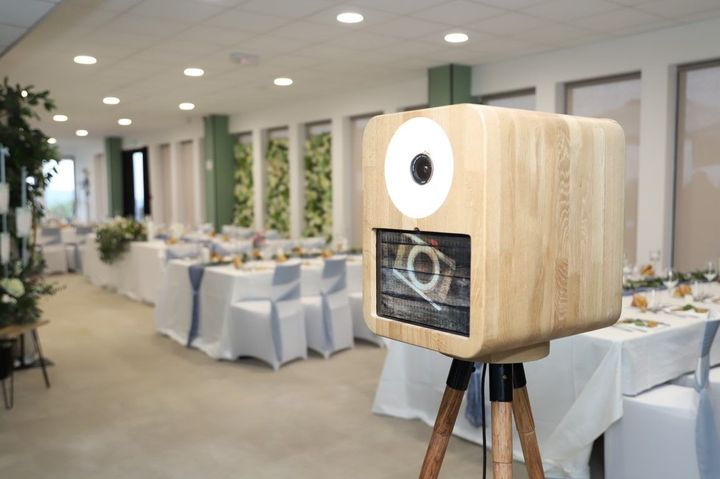 Wooden photo booth camera on a tripod in a bright banquet hall with white table settings