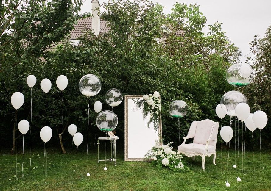 White balloon-decorated garden with a chair, mirror, and champagne glasses on the grass