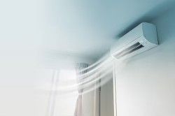 A wall mounted air conditioner is blowing air out of a window.