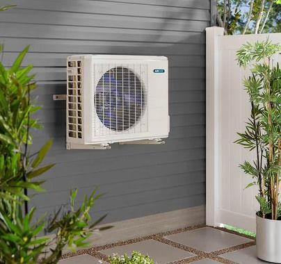 A white air conditioner is mounted on a wall next to a potted plant.