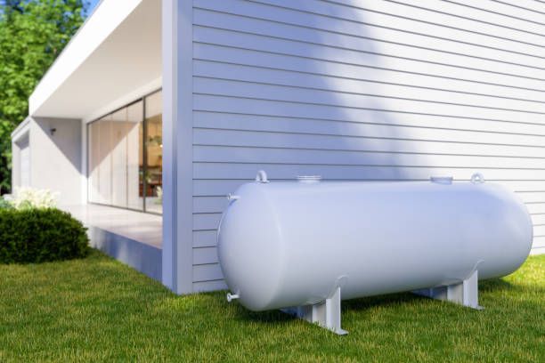 A large white propane tank is sitting in the grass in front of a house.
