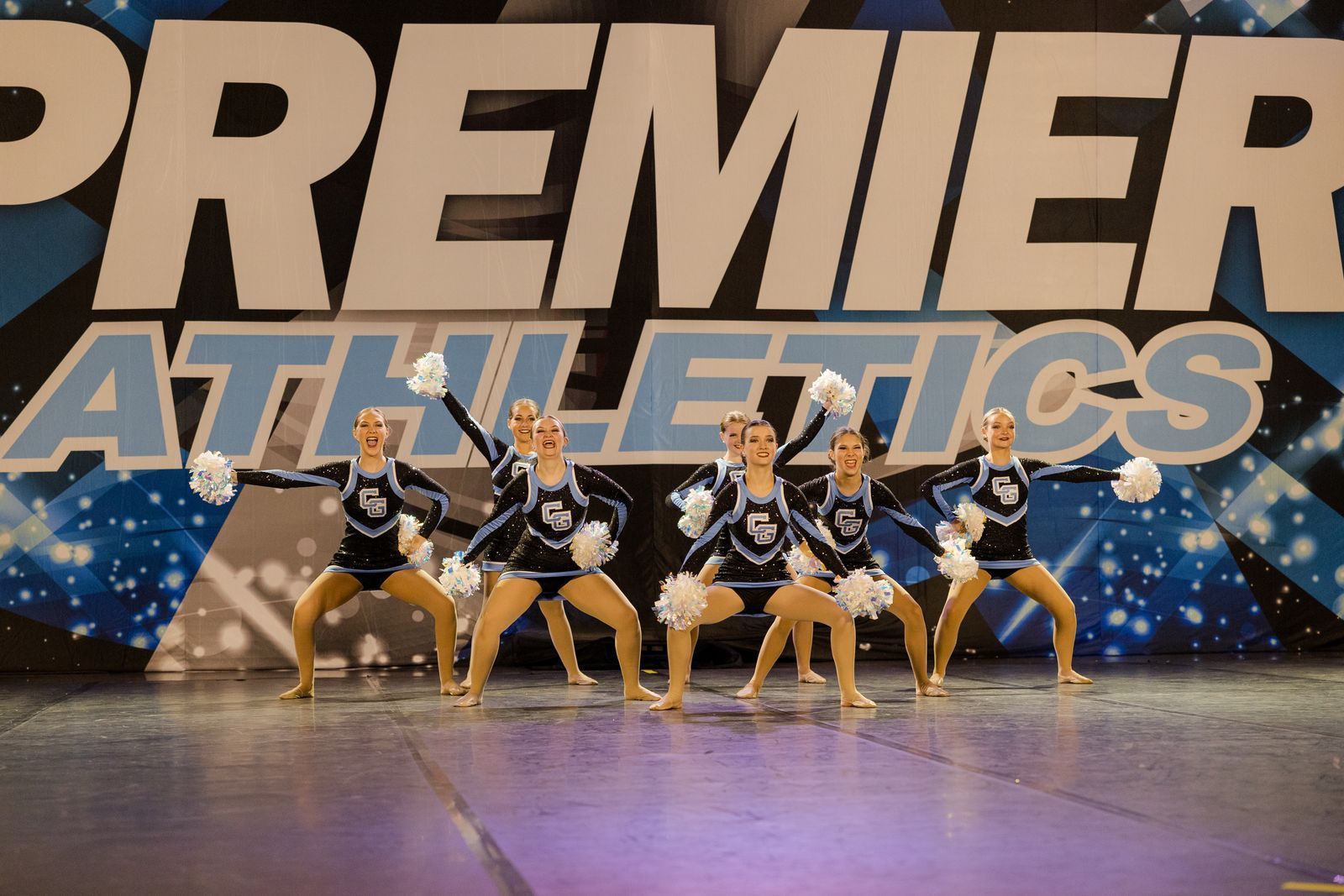 A group of cheerleaders are performing in front of a premier athletics sign