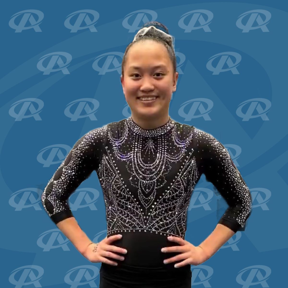 A woman stands with her hands on her hips in front of a blue background with the letter r on it