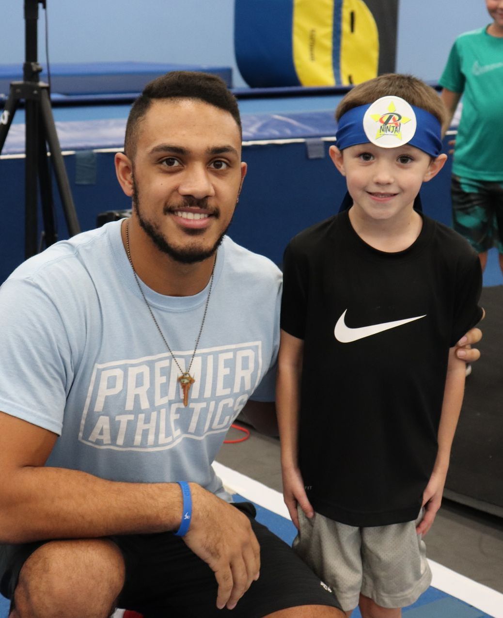 A man wearing a premier athletics shirt sits next to a young boy