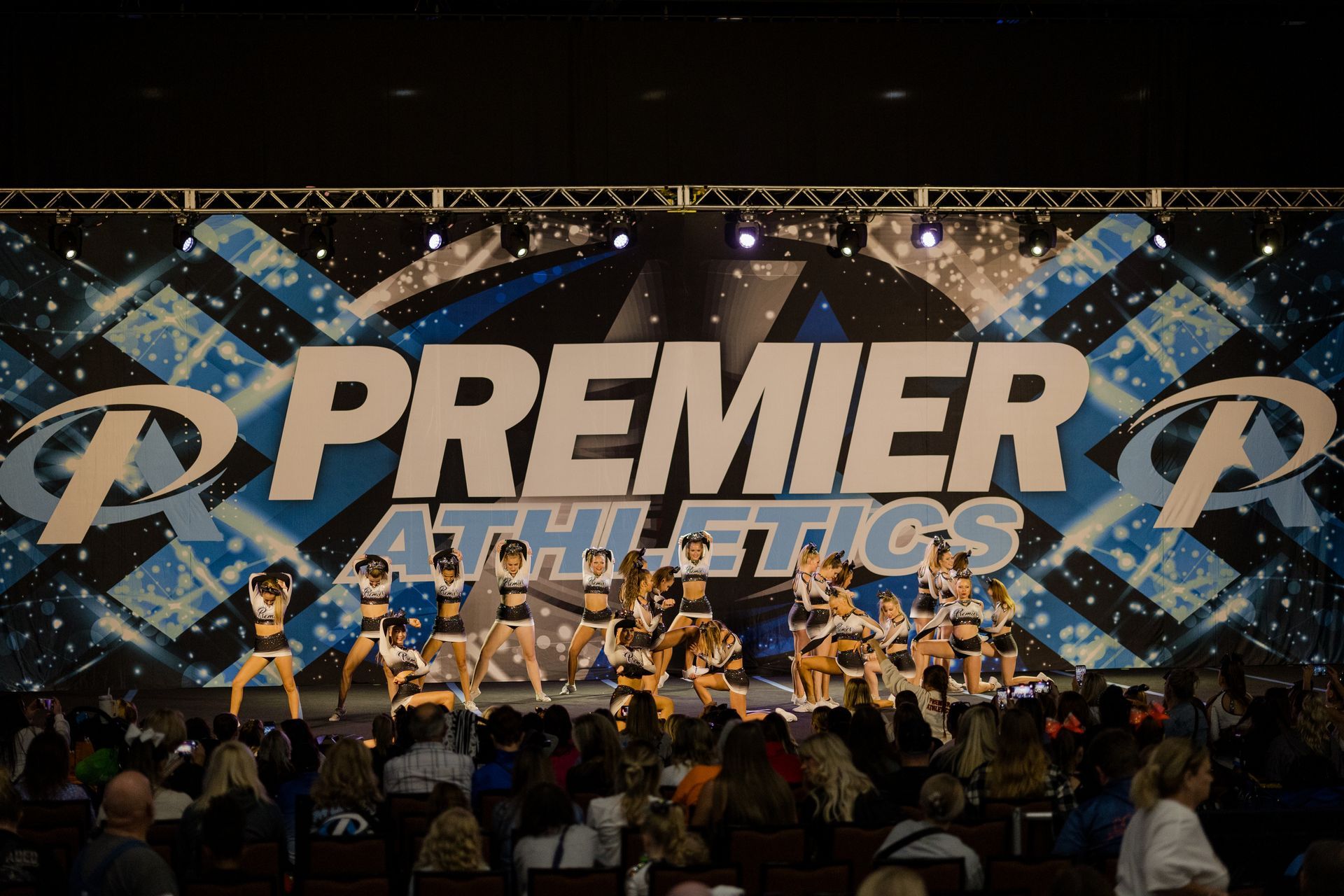 A group of cheerleaders are performing in front of a large screen that says premier athletics