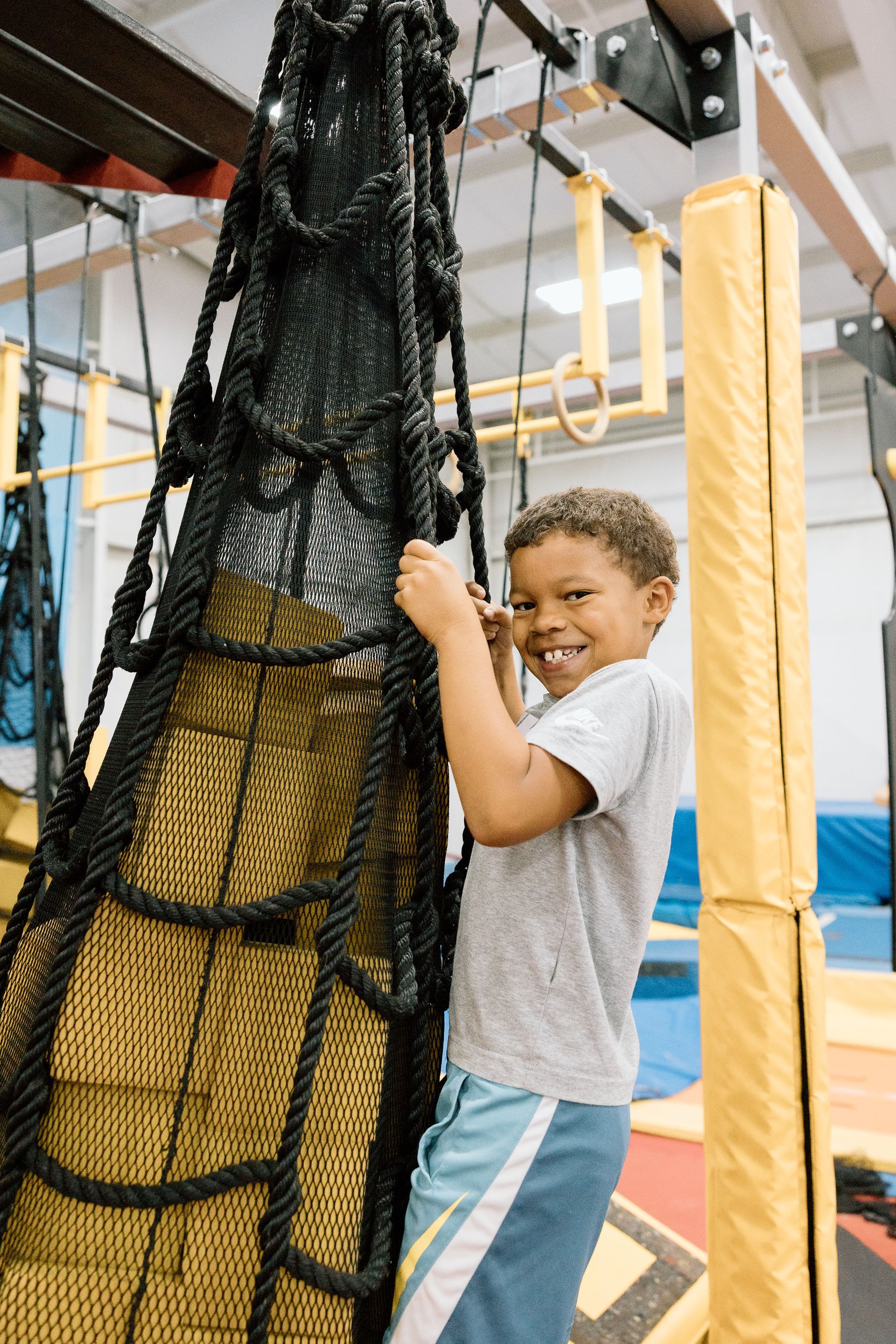 A young boy is climbing a rope ladder in a gym.