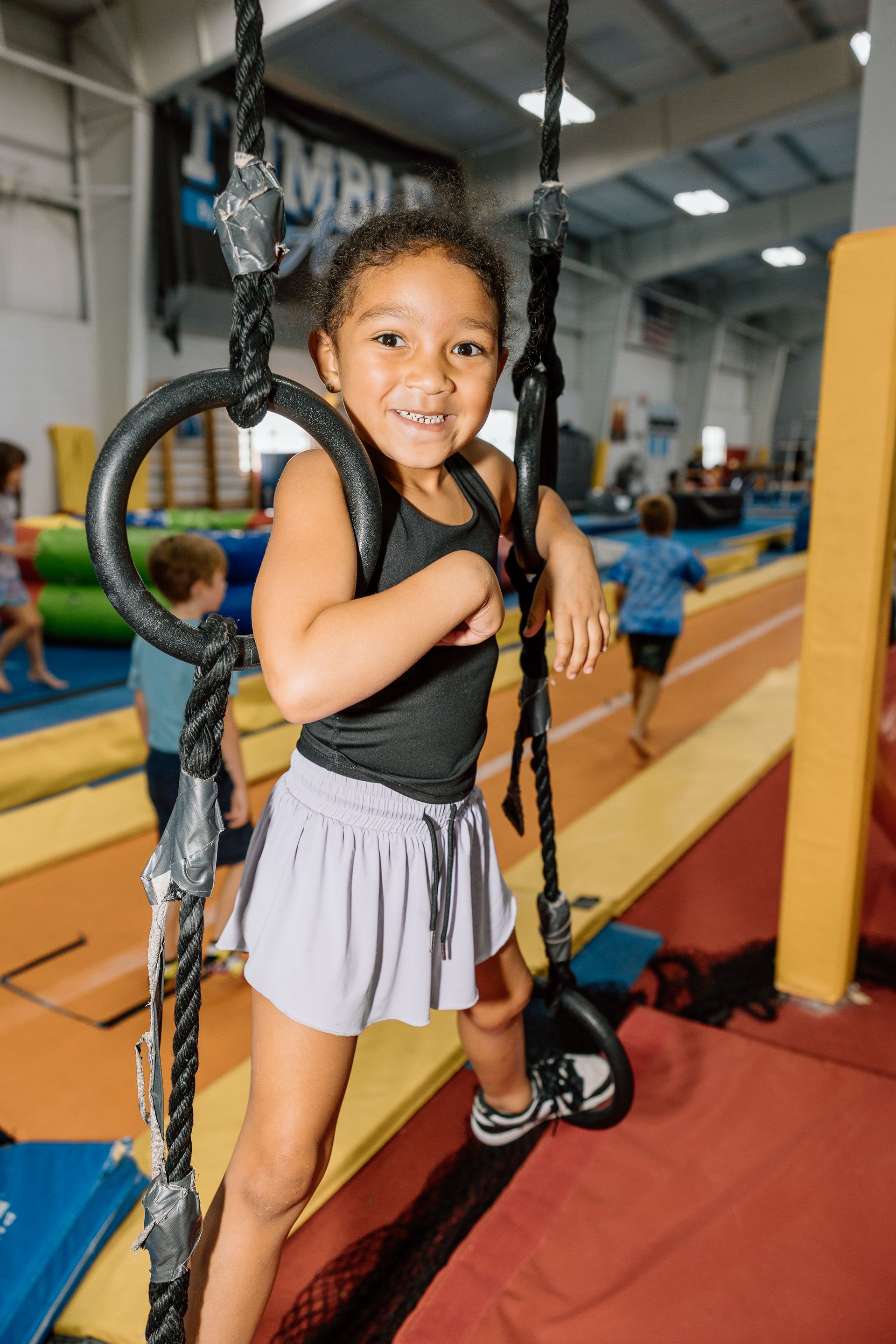 A little girl is standing on a rope swing in a gym.