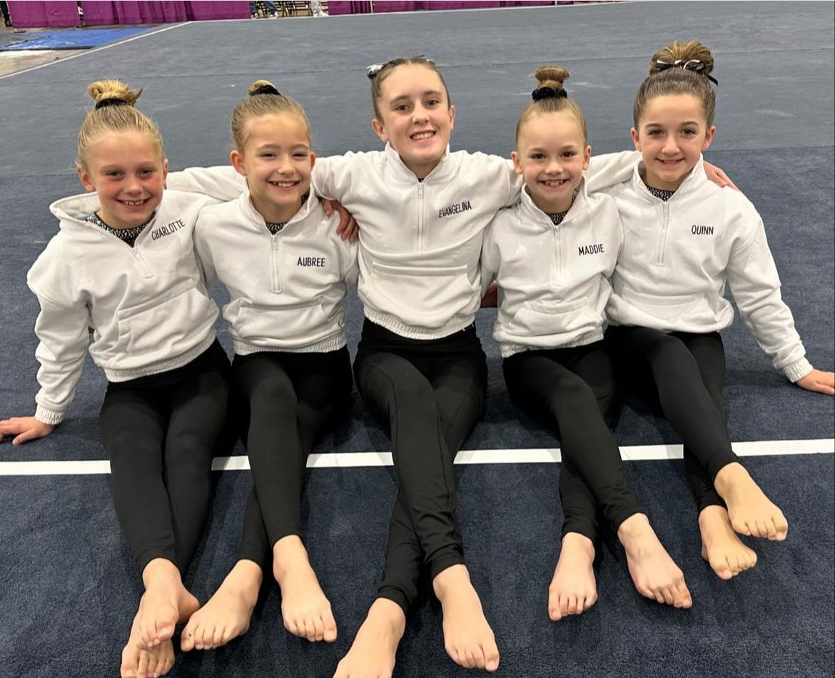A group of young girls are posing for a picture while sitting on the floor.