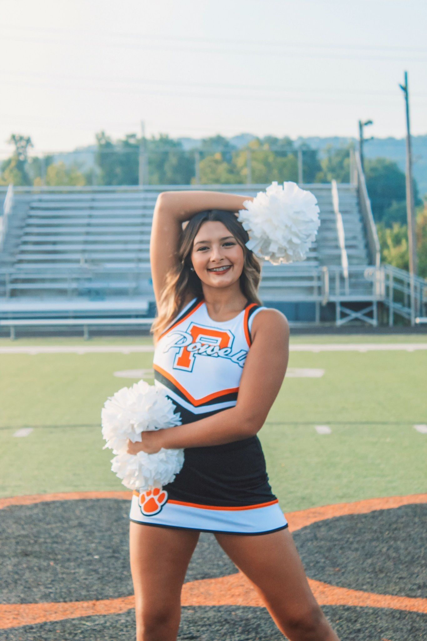 A cheerleader is holding pom poms on a football field.