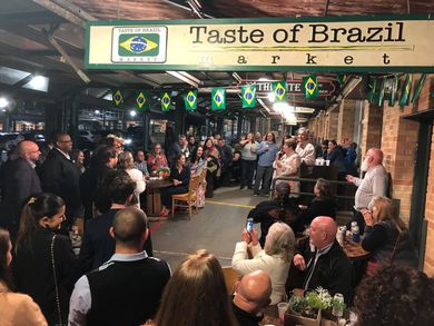 A group of people are gathered under a sign that says taste of brazil