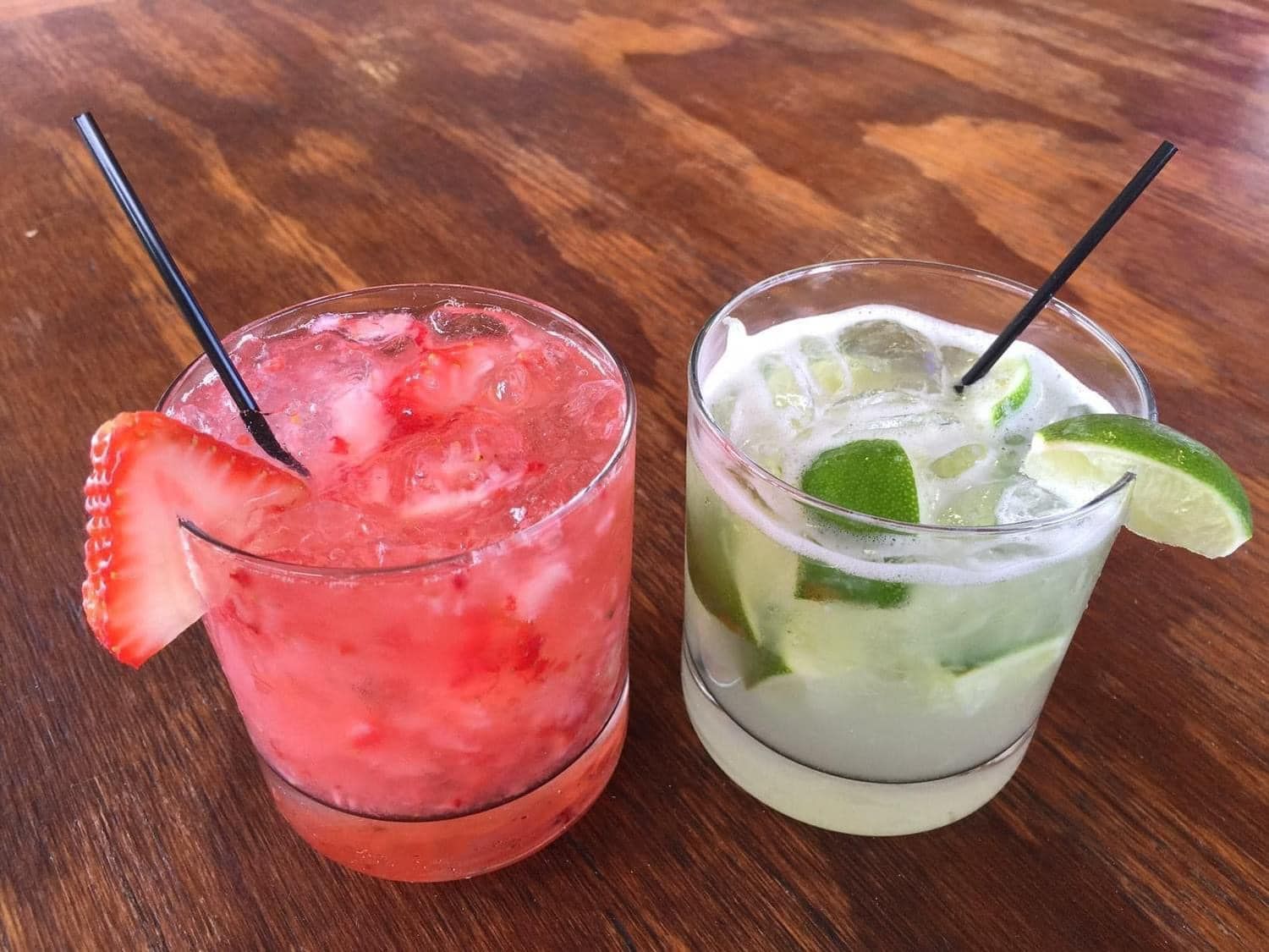 Two drinks on a wooden table with straws in them