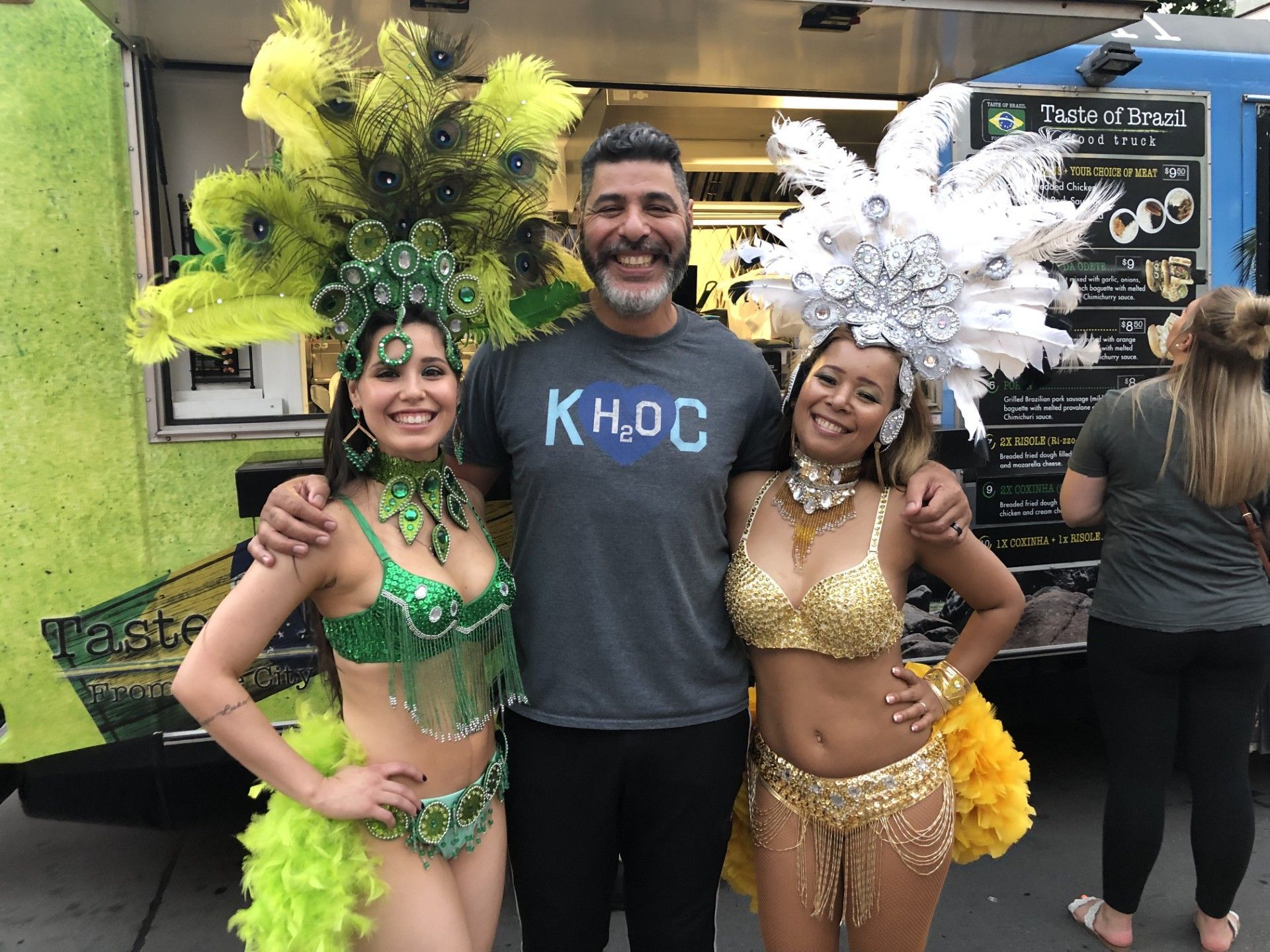 A man and two women are posing for a picture in front of a food truck.
