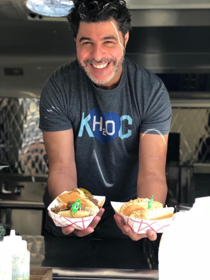 A man wearing a khoc shirt is holding two plates of food in his hands