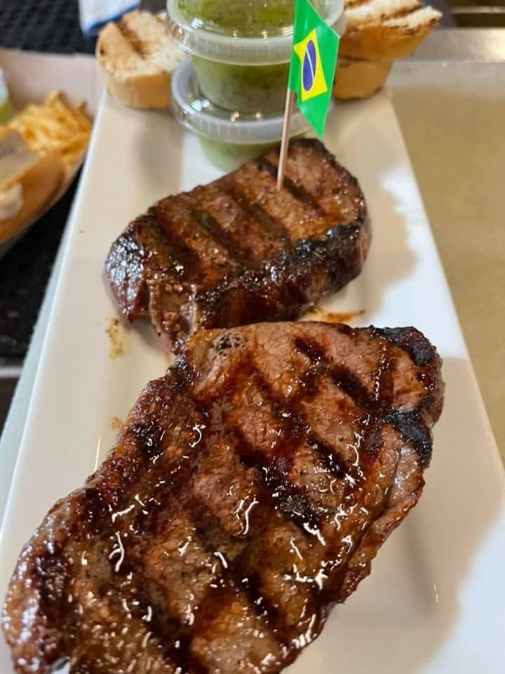 Two grilled steaks on a white plate with a toothpick in the middle.