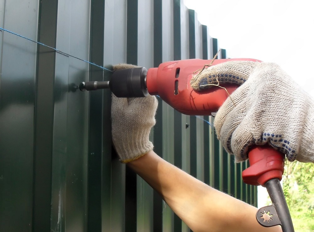 a person is using a drill on a green fence