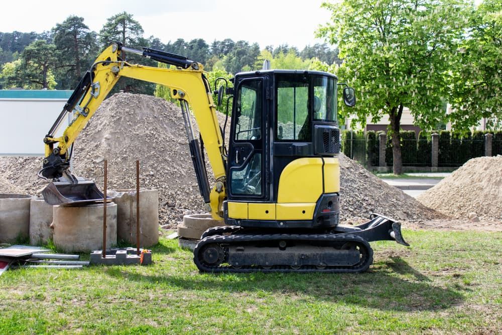 A Yellow Excavator Is Parked in A Grassy Field Next to A Pile of Dirt — Albury Demolitions in Lavington, NSW