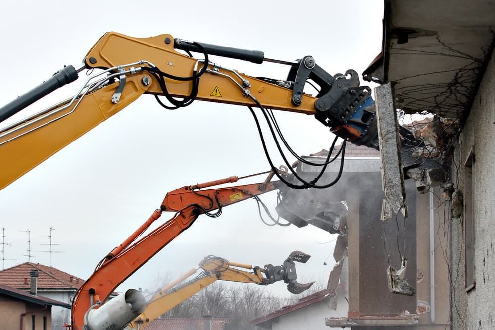 A Yellow and Orange Excavator Is Demolishing a Building — Albury Demolitions in Lavington, NSW