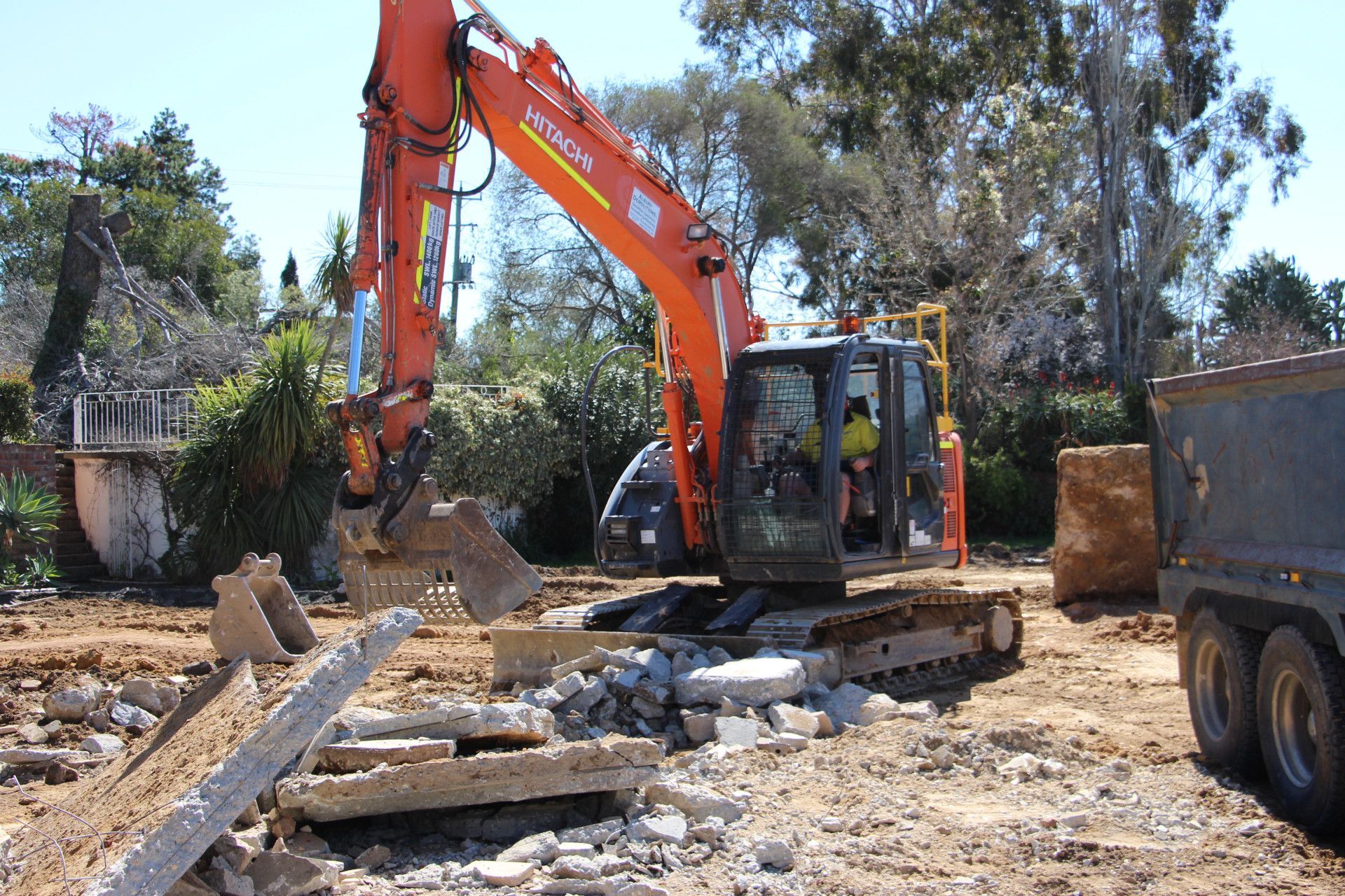 A Yellow Excavator Is Working on A Construction Site in Front of A Building — Albury Demolitions in Lavington, NSW