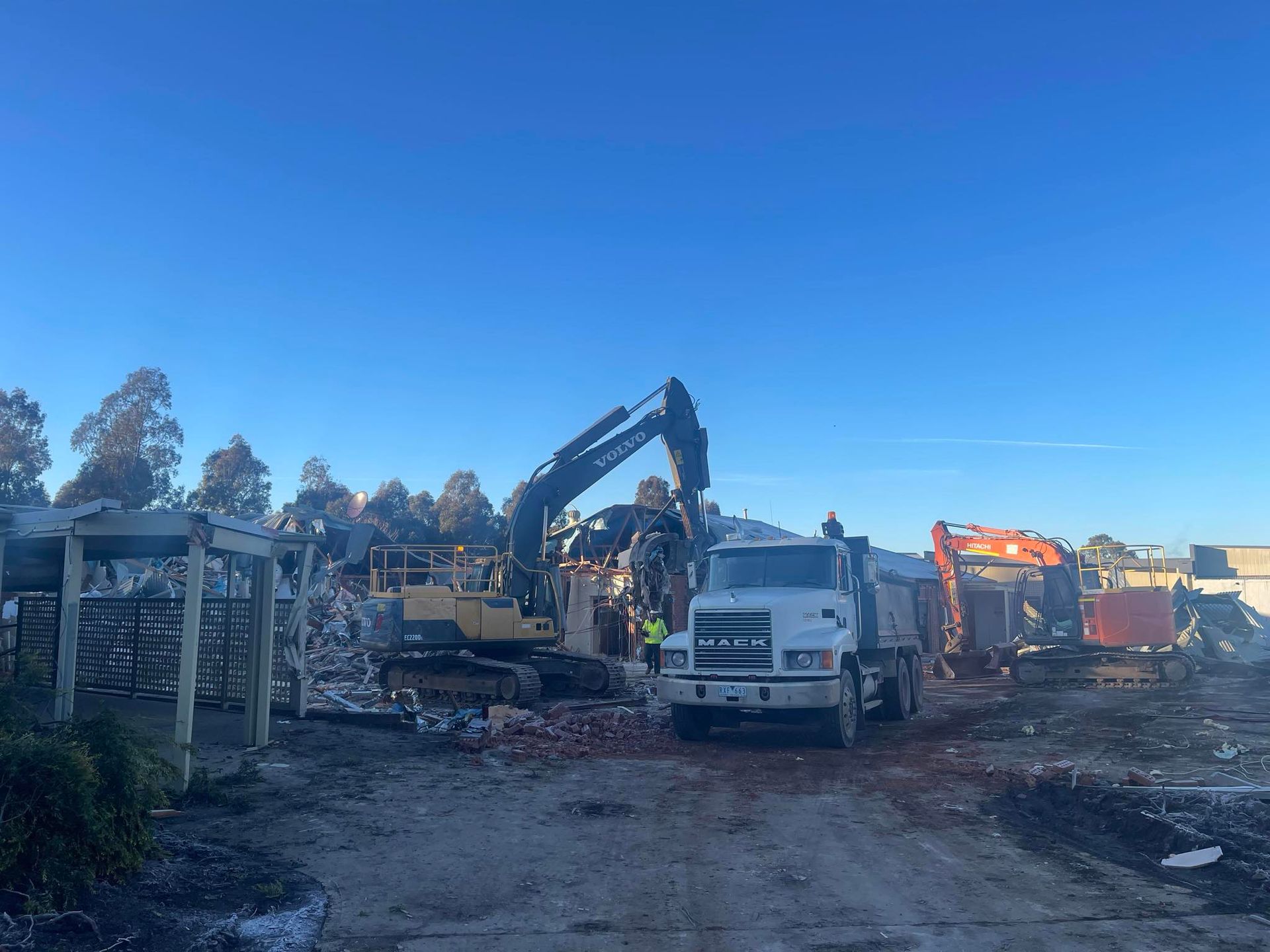A Yellow Excavator Is Working on A Construction Site in Front of A Building — Albury Demolitions in Holbrook, NSW