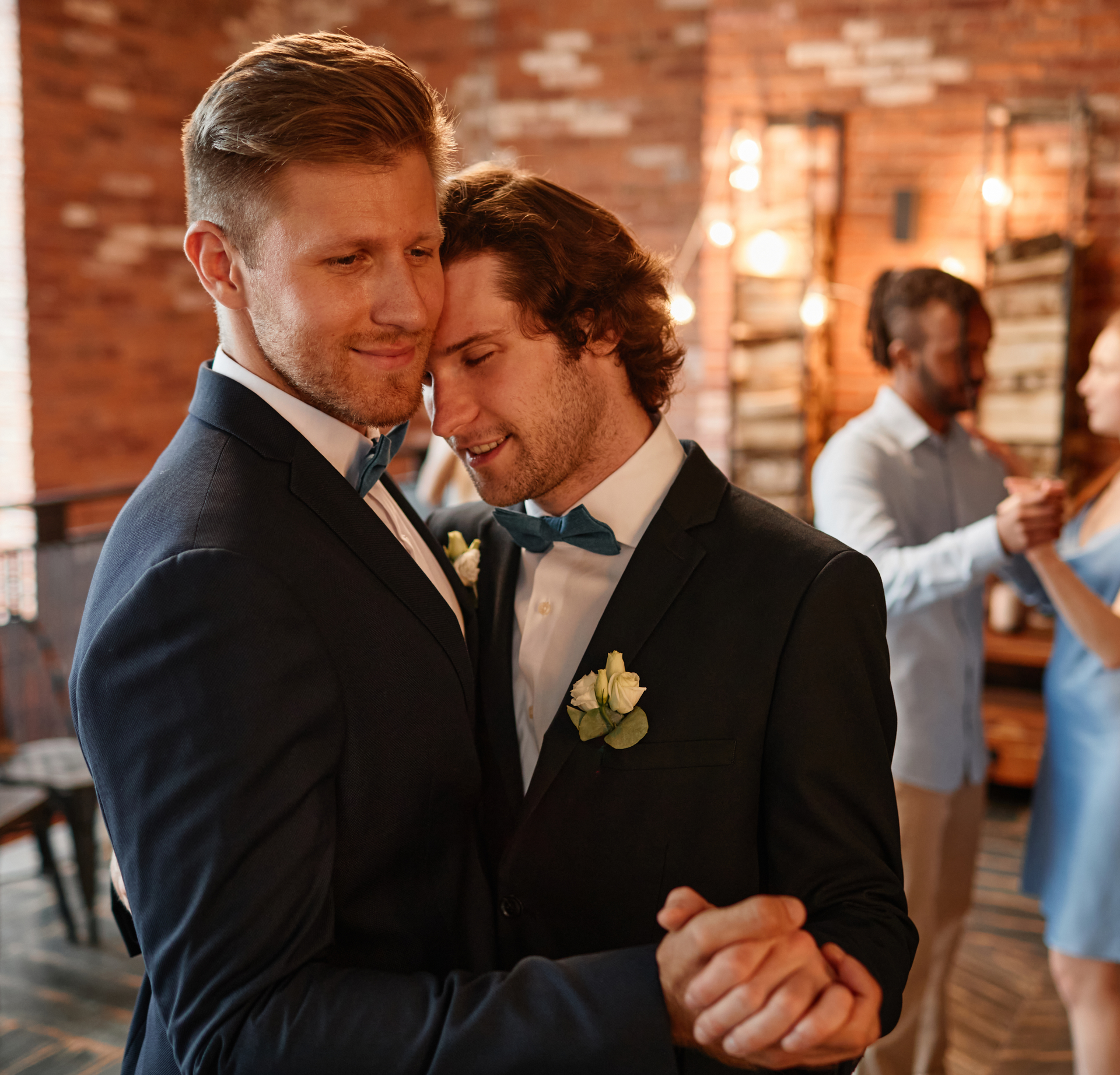 Two men in suits and bow ties are dancing together at a wedding reception.
