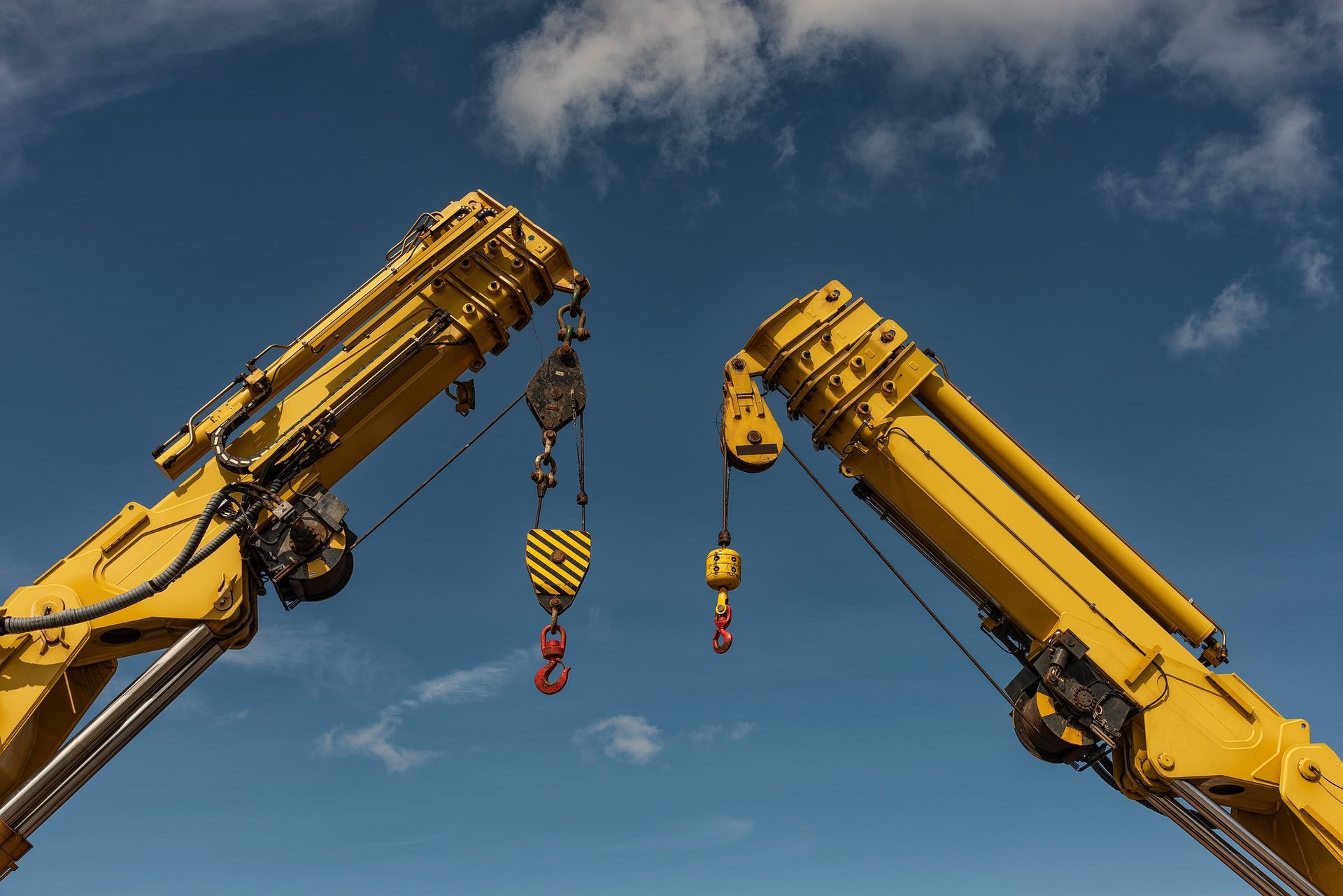 Two yellow crane arms with hooks against a blue sky with clouds. Two yellow crane arms with hooks against a blue sky with clouds.