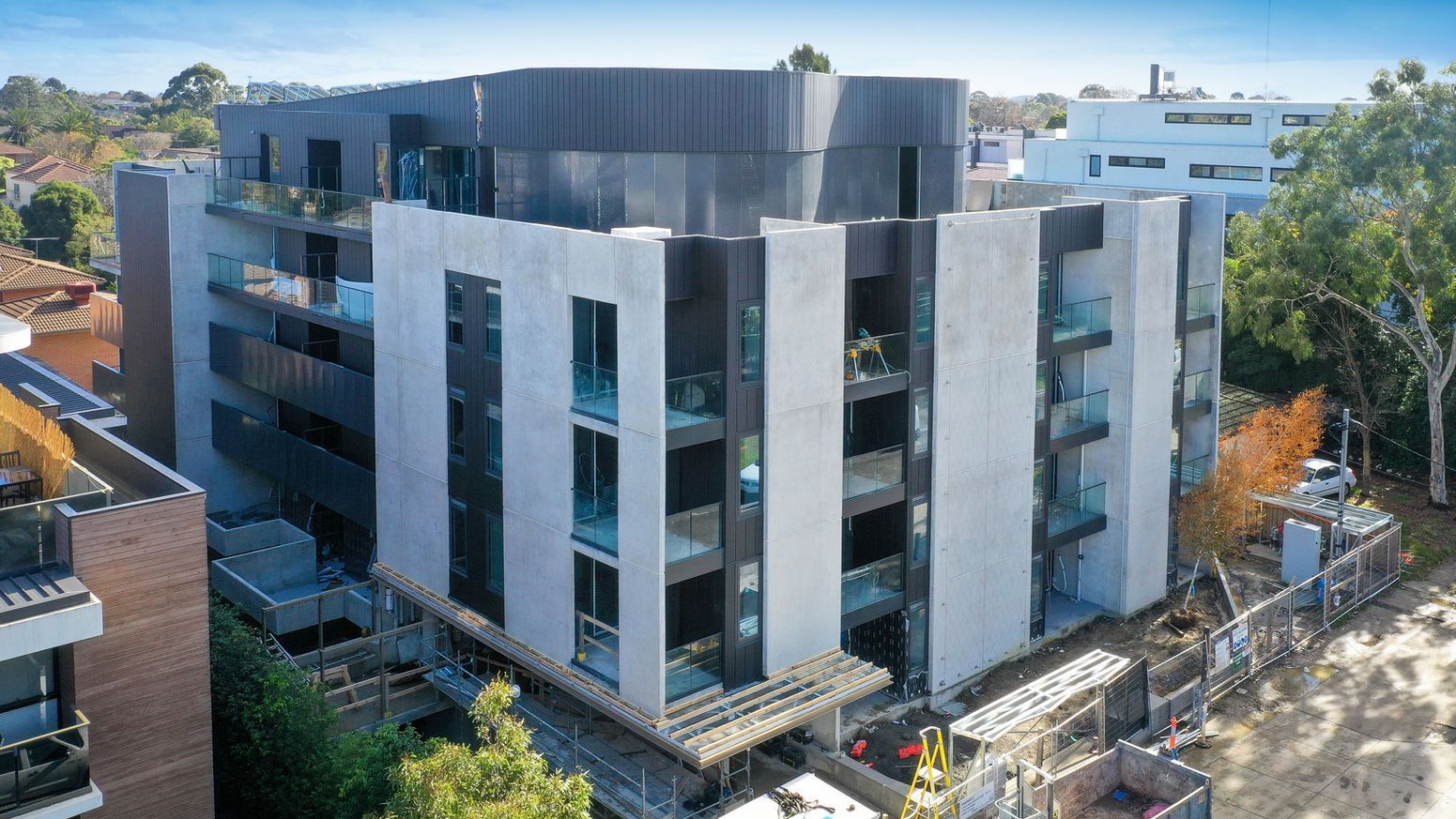 Modern apartment building with concrete and dark metal facade, under construction.