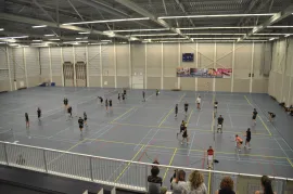 Een opname vanuit een hoog perspectief van een grote overdekte sporthal met mensen die trainen op een gemarkeerd grijs veld.