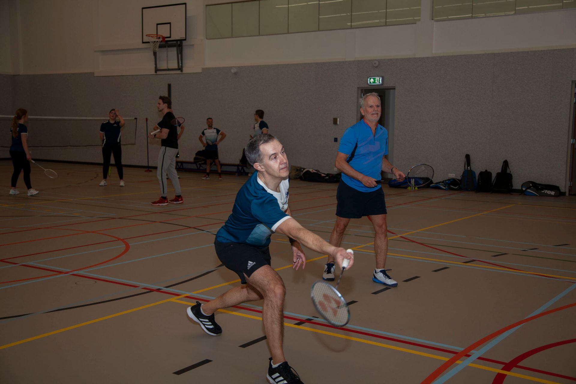 Een persoon in een blauw shirt maakt een sprong om met een racket een shuttle te raken op een badmintonveld