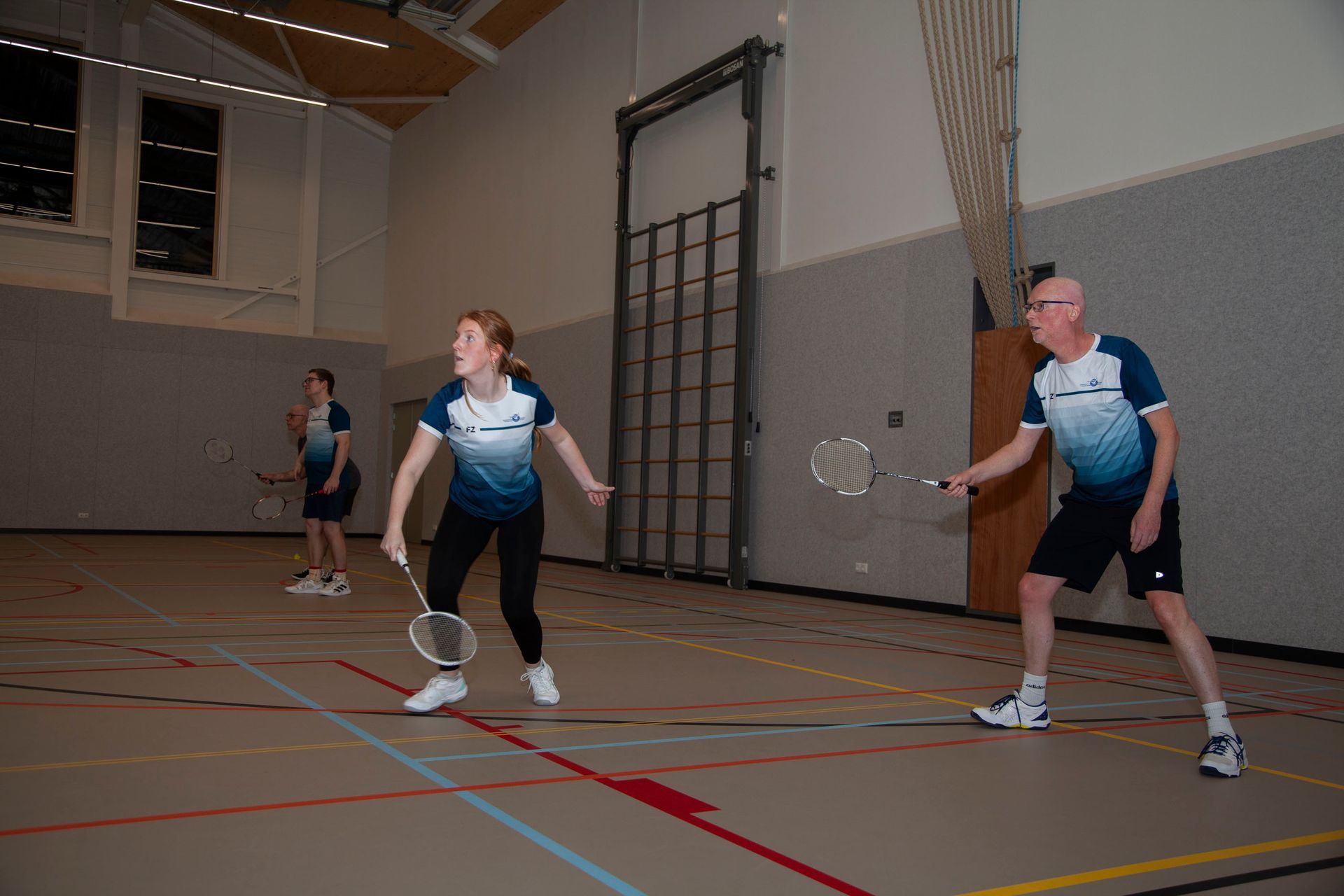 Drie mensen in bijpassende uniformen spelen badminton op een indoorbaan