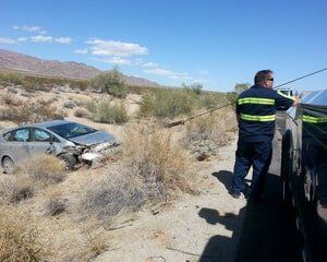 A tow truck operator pulls a damaged car out of desert brush.